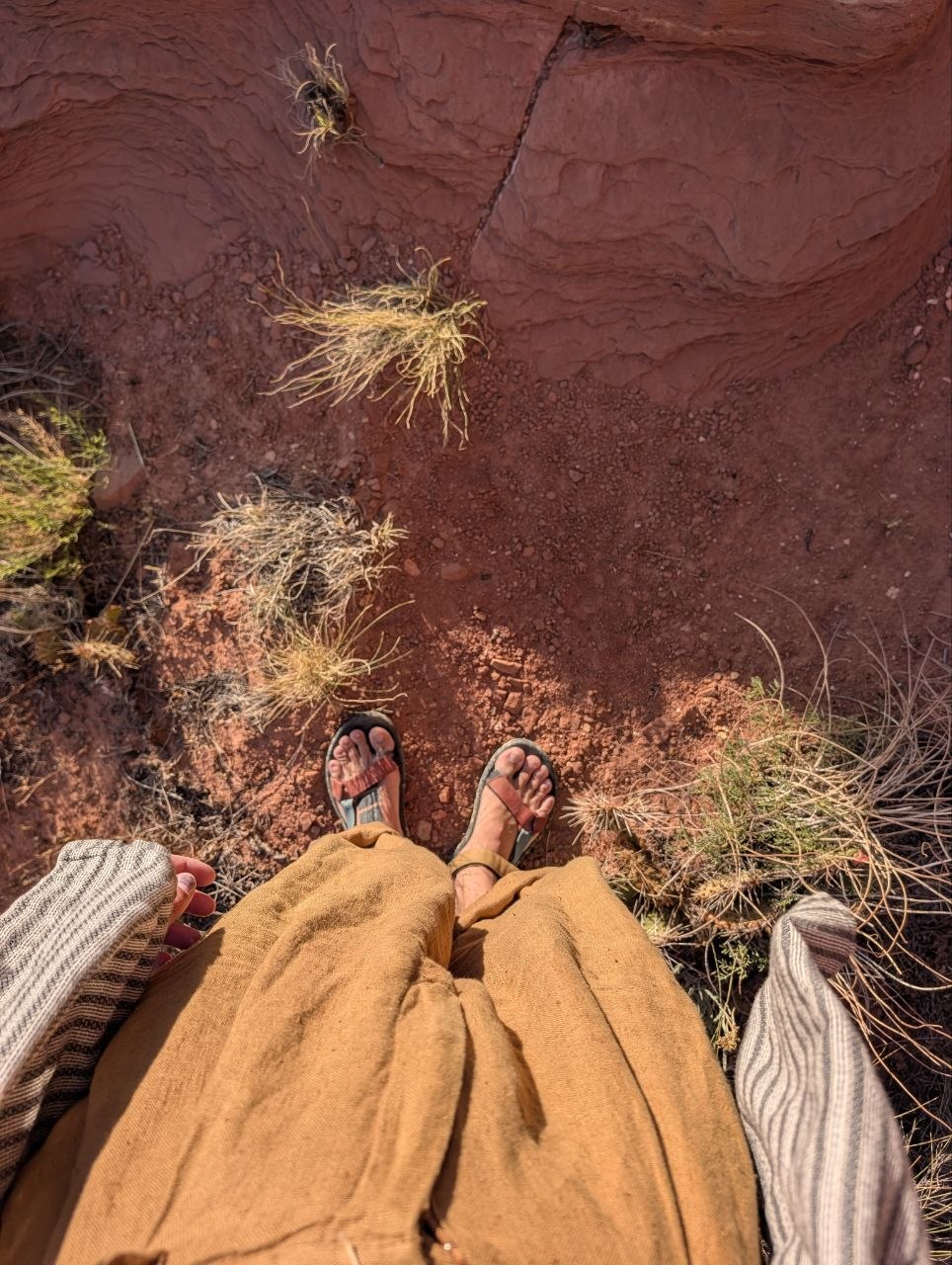 Sandaled feet and wide tan pants standing above red sandstone in the Escalante River corridor