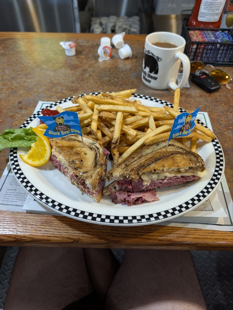 A Reuben sandwich with fries and two small Black Bear Diner flags on a plate