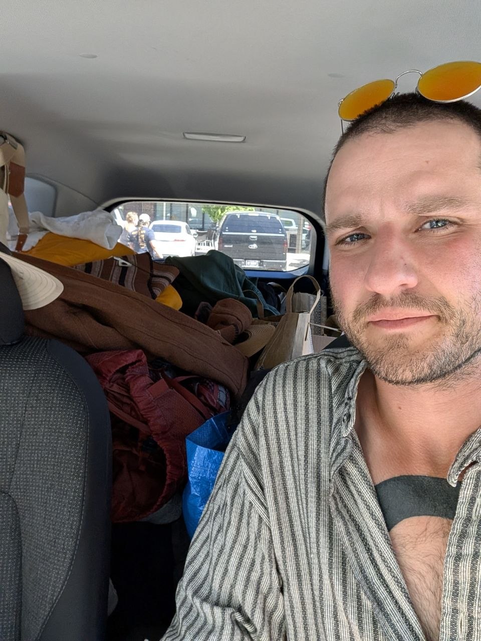 Cameron sitting in a packed road-trip car wearing yellow sunglasses on his head