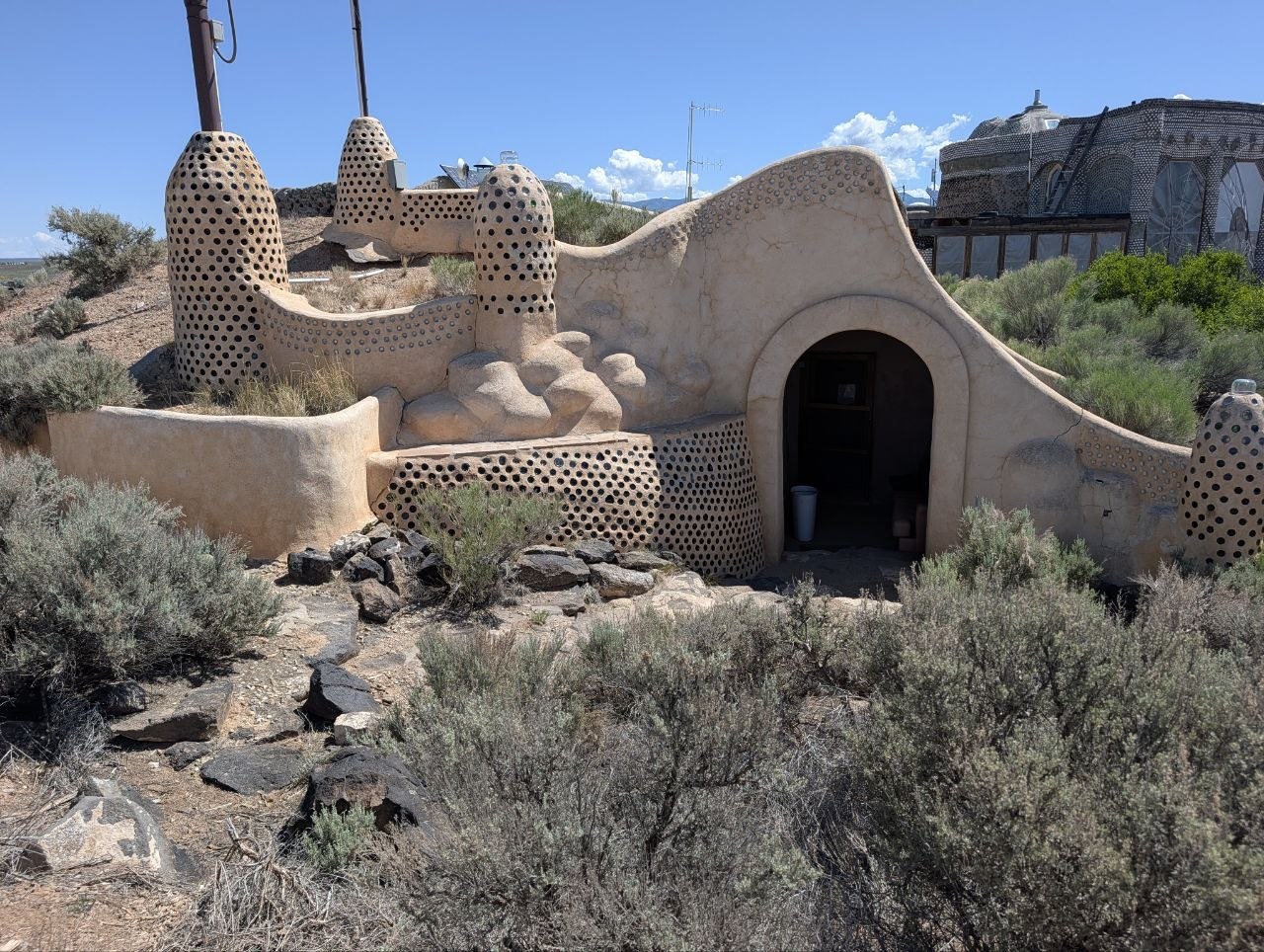 Curved adobe Earthship courtyard walls with bottle openings and desert scrub