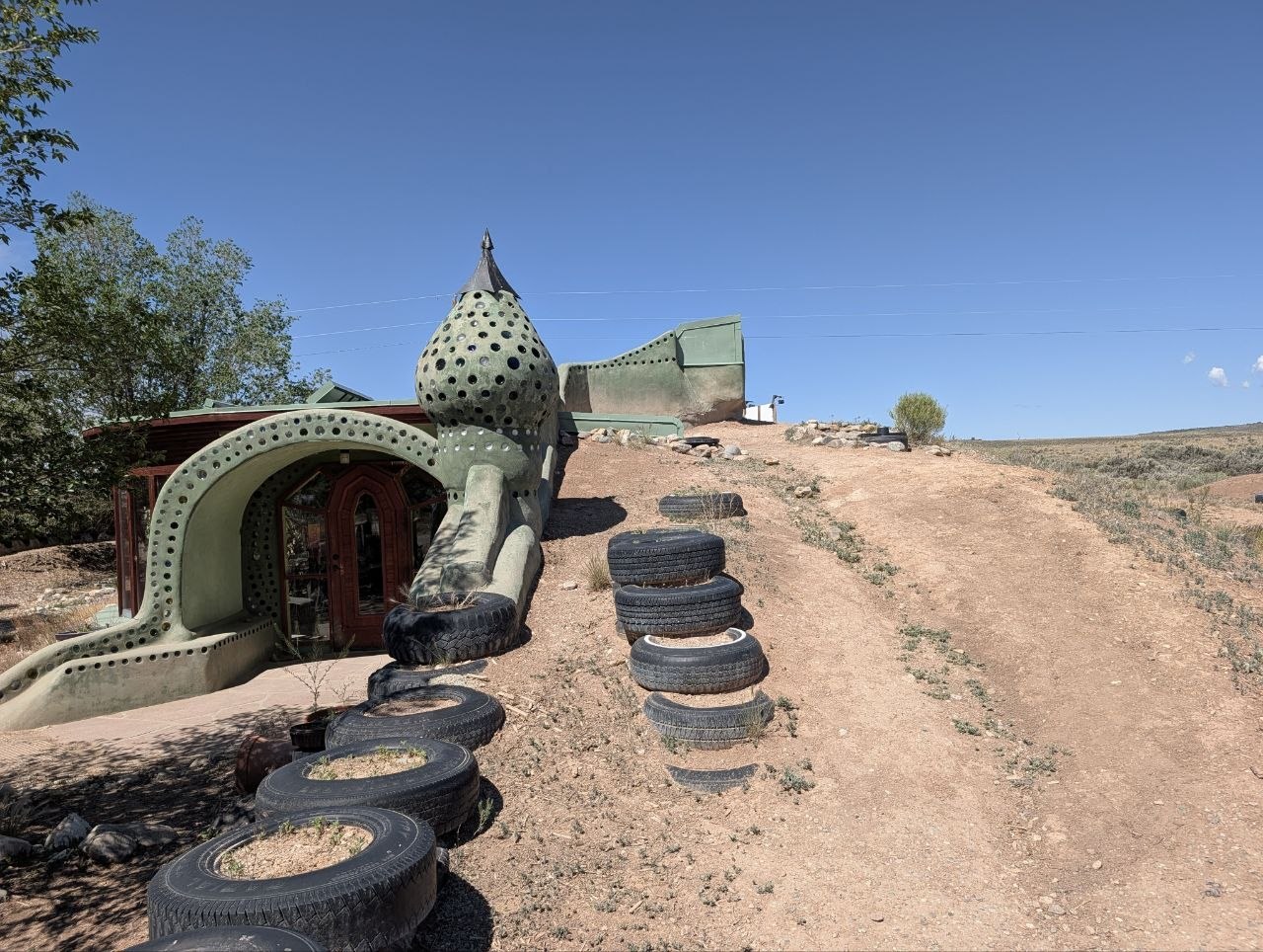 Curved Earthship entrance with tires and rounded towers on a dry desert slope