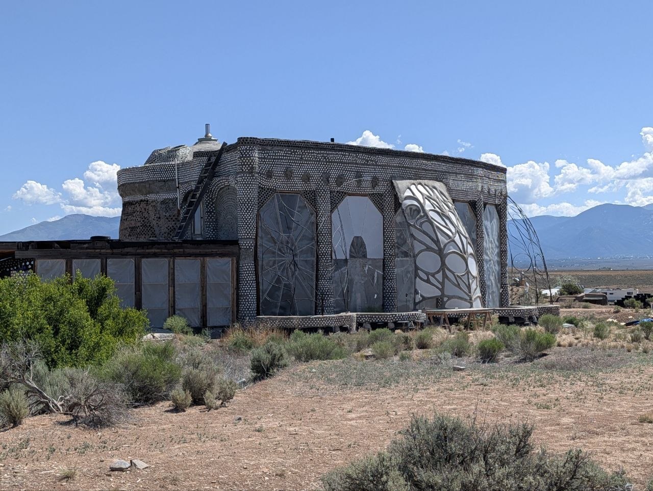 An Earthship building on the Taos mesa with bottle-pattern walls and mountains behind it