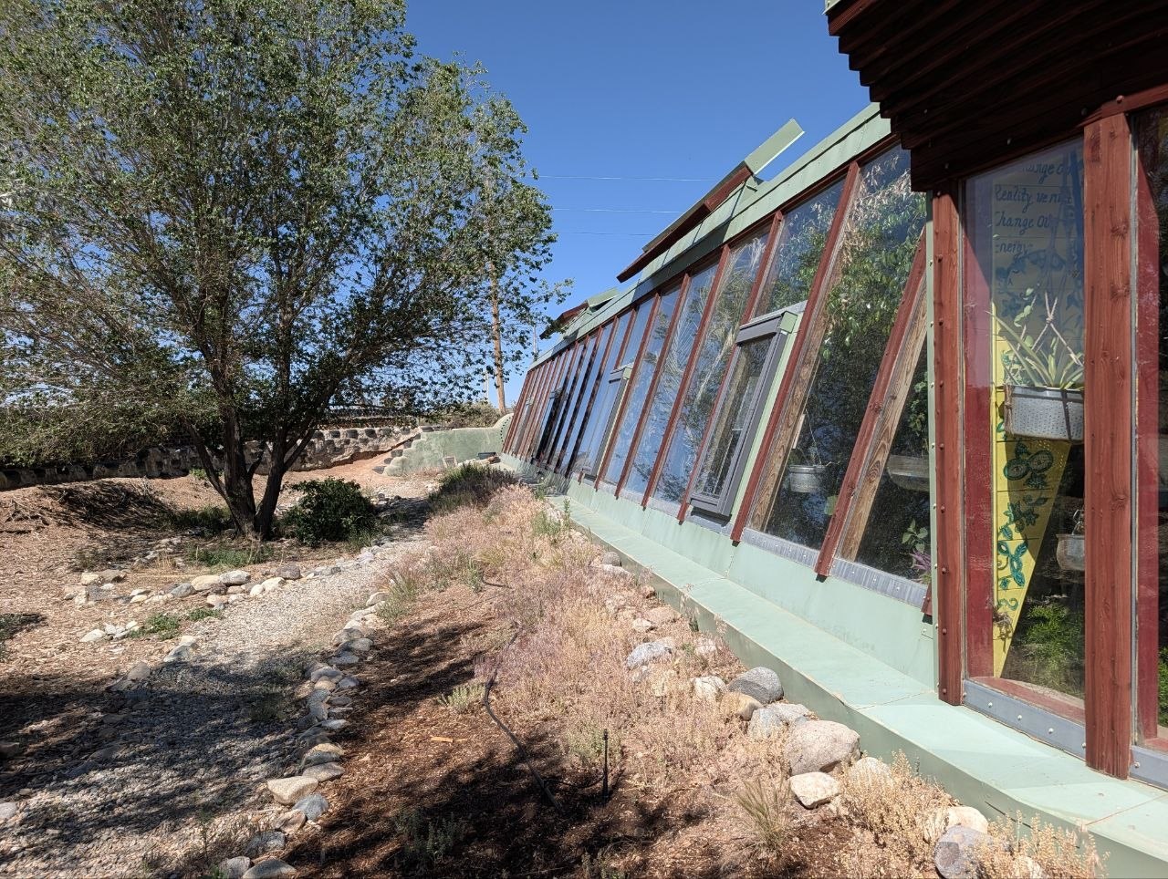 Exterior of an Earthship greenhouse wall with red wood framing and slanted glass
