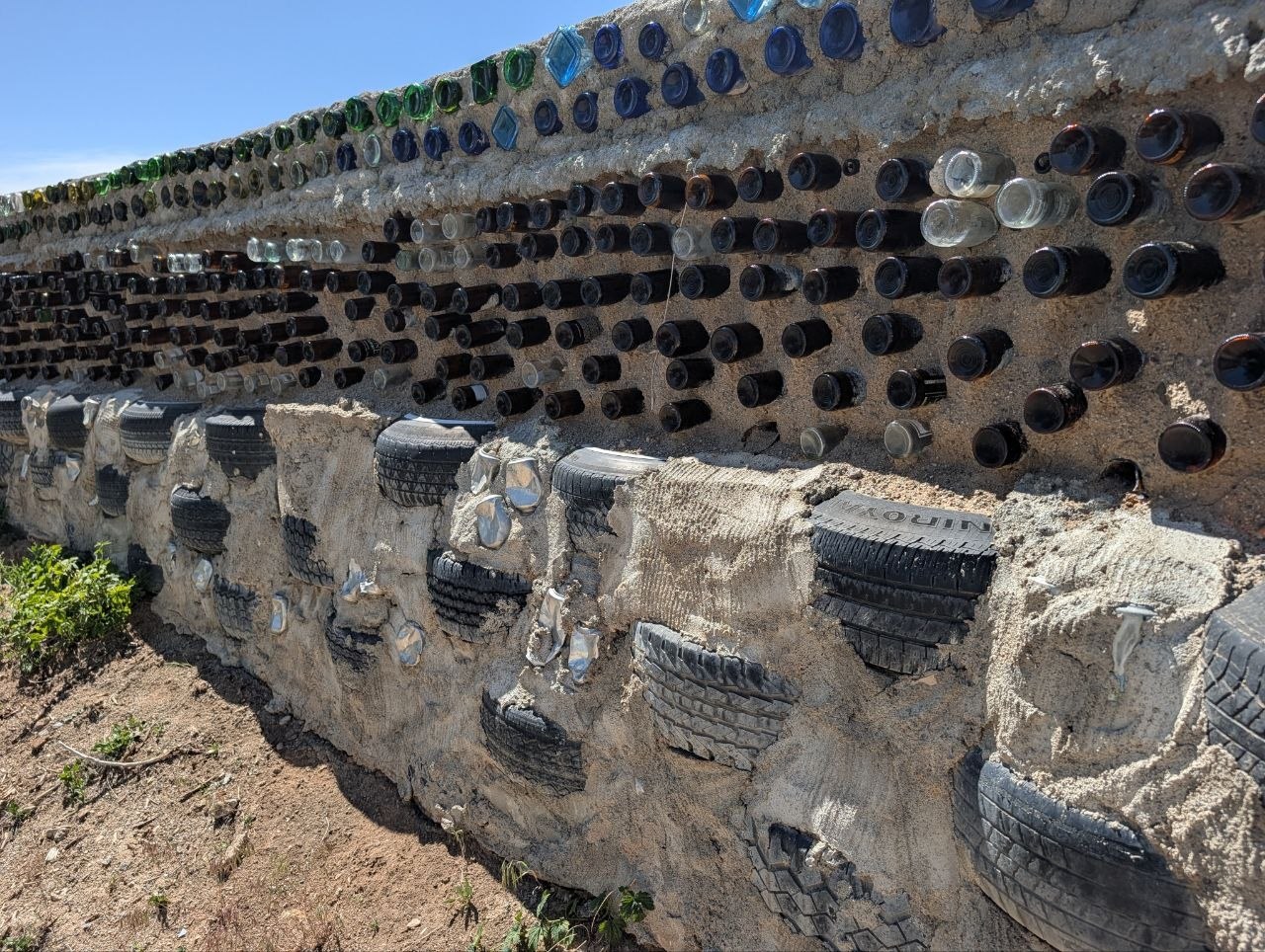 Earthship wall made from embedded bottles and tires under desert sun