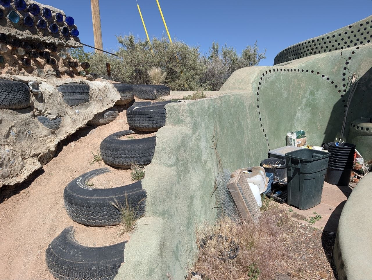 Tires used as steps and retaining structure beside curved adobe Earthship walls