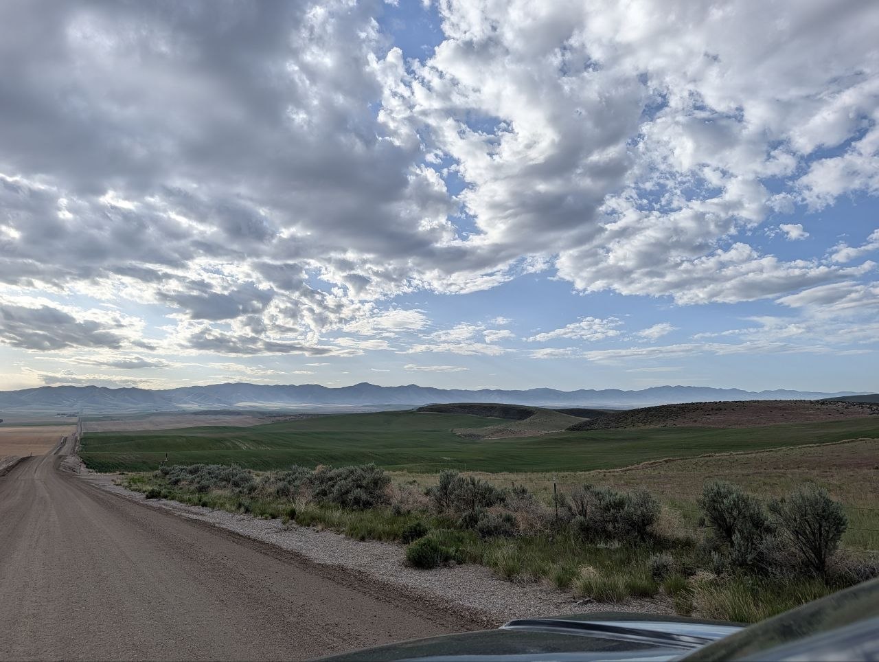A dirt road and open fields under dramatic clouds with mountains in the distance